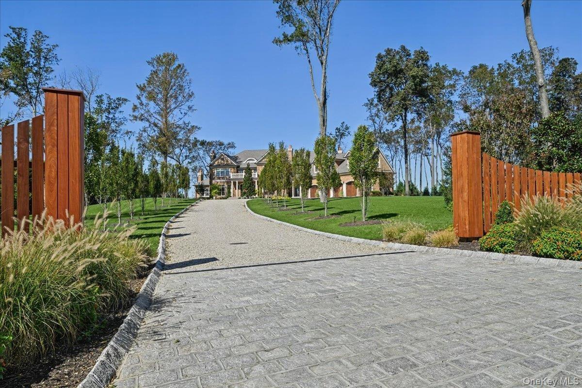 Paved driveway leading to a stone and brick exterior residence with a columned portico, surrounded by mature trees and manicured lawns