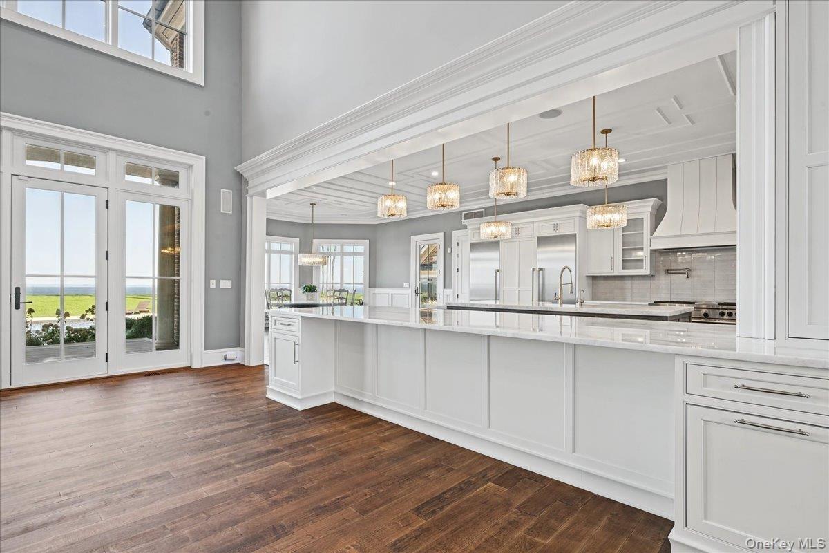 Spacious open-concept kitchen with wood-finish flooring, white cabinetry, a large kitchen island, and multiple pendant lights
