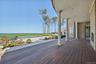 Expansive outdoor deck with dark wood-finish flooring, brick exterior, and white columns