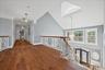 Hardwood flooring, wrought iron railing with wood-finish top, white wainscoting, recessed lighting, and a vaulted ceiling with skylight