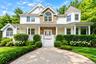 Classic Colonial-style residence featuring a brick and stone facade with white siding, arched entryway with decorative transom window, and a covered f
