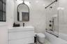 Floating vanity with integrated sink, black-framed arched mirror, black matte fixtures, and full-height wall tiling