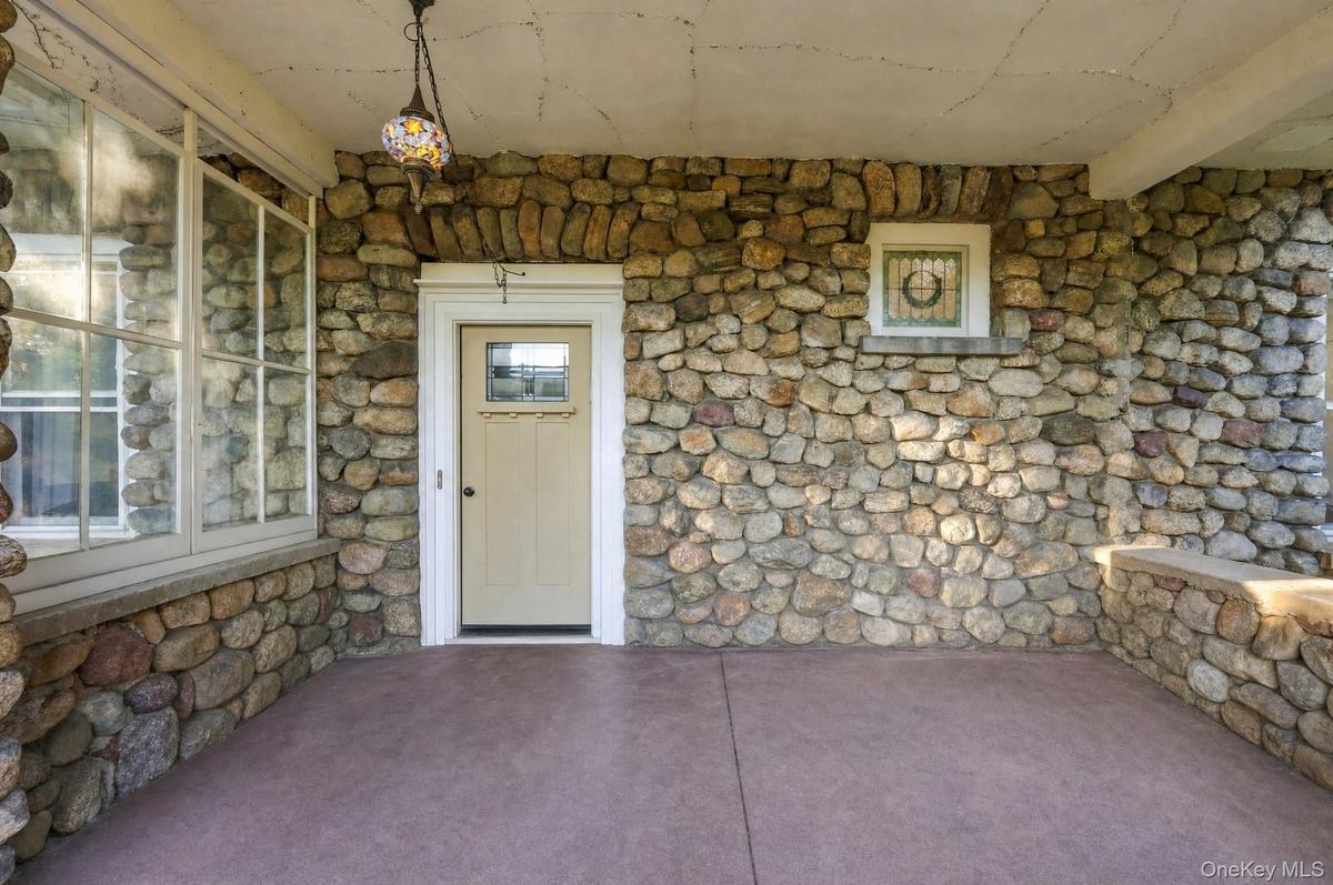 Stone exterior wall with a light-colored entry door featuring a window insert, multi-pane windows