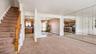 Carpeted staircase with wood railing, wall-mounted mirrored panels, and visible kitchen with wood-finish cabinetry