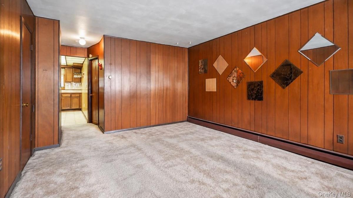 Wood-panel walls, wall-to-wall carpeting, and a visible kitchen entry