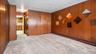 Wood-panel walls, wall-to-wall carpeting, and a visible kitchen entry