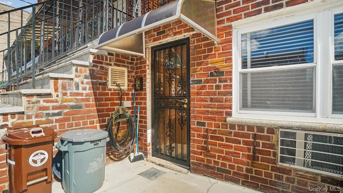 Brick exterior with a security screen door, decorative metal railing, exterior lighting, and a window air conditioning unit