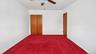 Room featuring red carpeting, white painted walls, a ceiling fan, and wood-finish doors