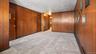 Wall paneling with a rich wood tone, light gray carpeting, and white ceiling finish