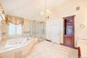 Jetted soaking tub with tile surround, glass-enclosed shower, built-in shelving, and chandelier lighting