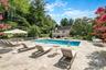 Expansive hardscape patio featuring a resort-style saltwater swimming pool with integrated spa, multiple lounge chairs, and market umbrellas