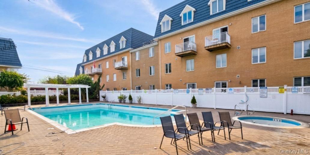 Outdoor swimming pool with integrated hot tub, surrounded by a brick paver patio and a white privacy fence