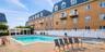 Outdoor swimming pool with integrated hot tub, surrounded by a brick paver patio and a white privacy fence