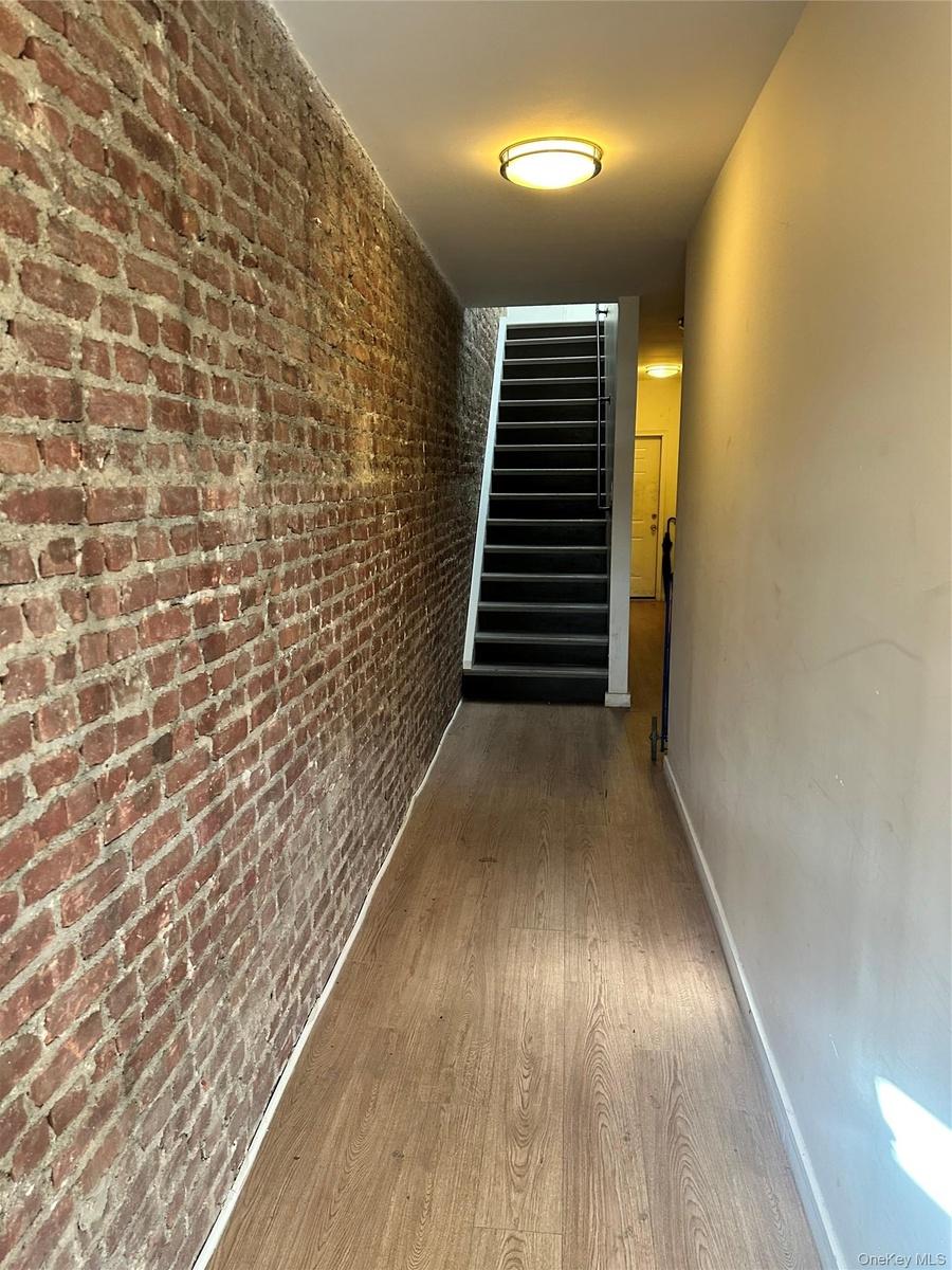 Exposed brick wall detail, wood-finish flooring, staircase with dark treads, and flush-mount ceiling lighting