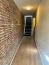 Exposed brick wall detail, wood-finish flooring, staircase with dark treads, and flush-mount ceiling lighting