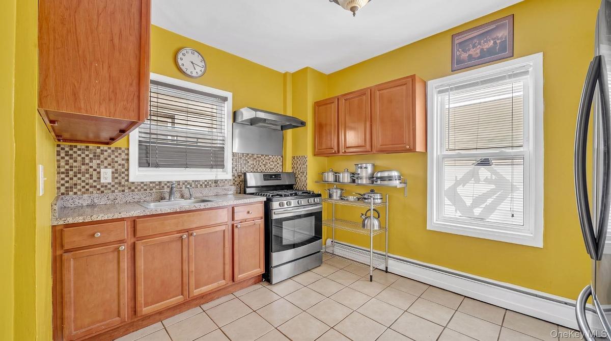 Kitchen featuring wood cabinetry, granite-style countertops, tile backsplash, and stainless steel appliances