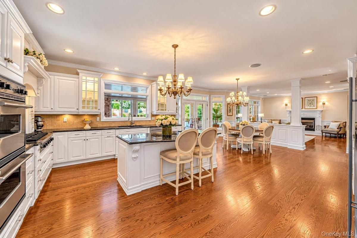 Gourmet kitchen featuring white cabinetry with glass-front doors, stainless steel double wall ovens, a large island with seating, quartz countertops, 