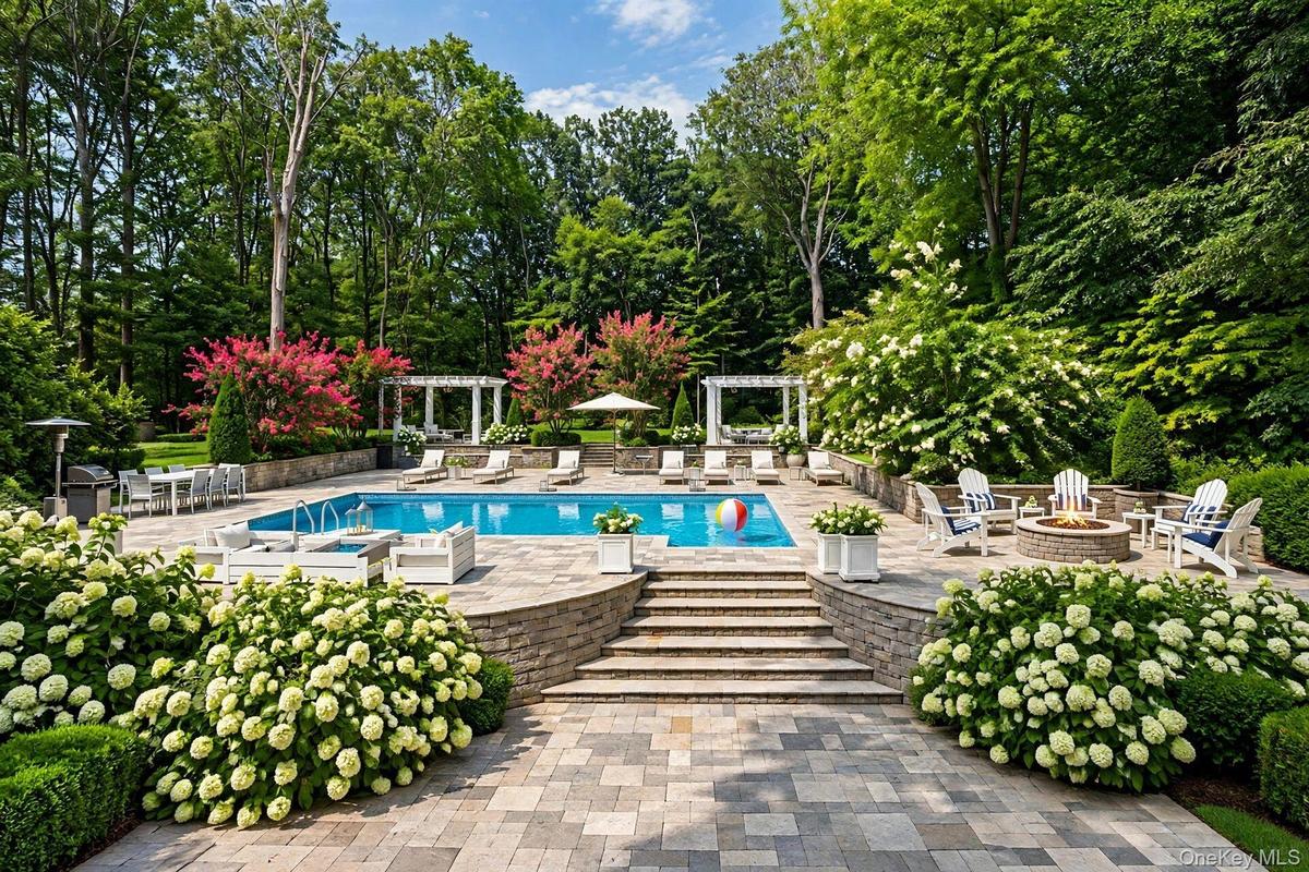 Expansive outdoor living area featuring a swimming pool, stone paver patio, integrated fire pit, and tiered landscaping