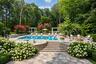 Expansive outdoor living area featuring a swimming pool, stone paver patio, integrated fire pit, and tiered landscaping
