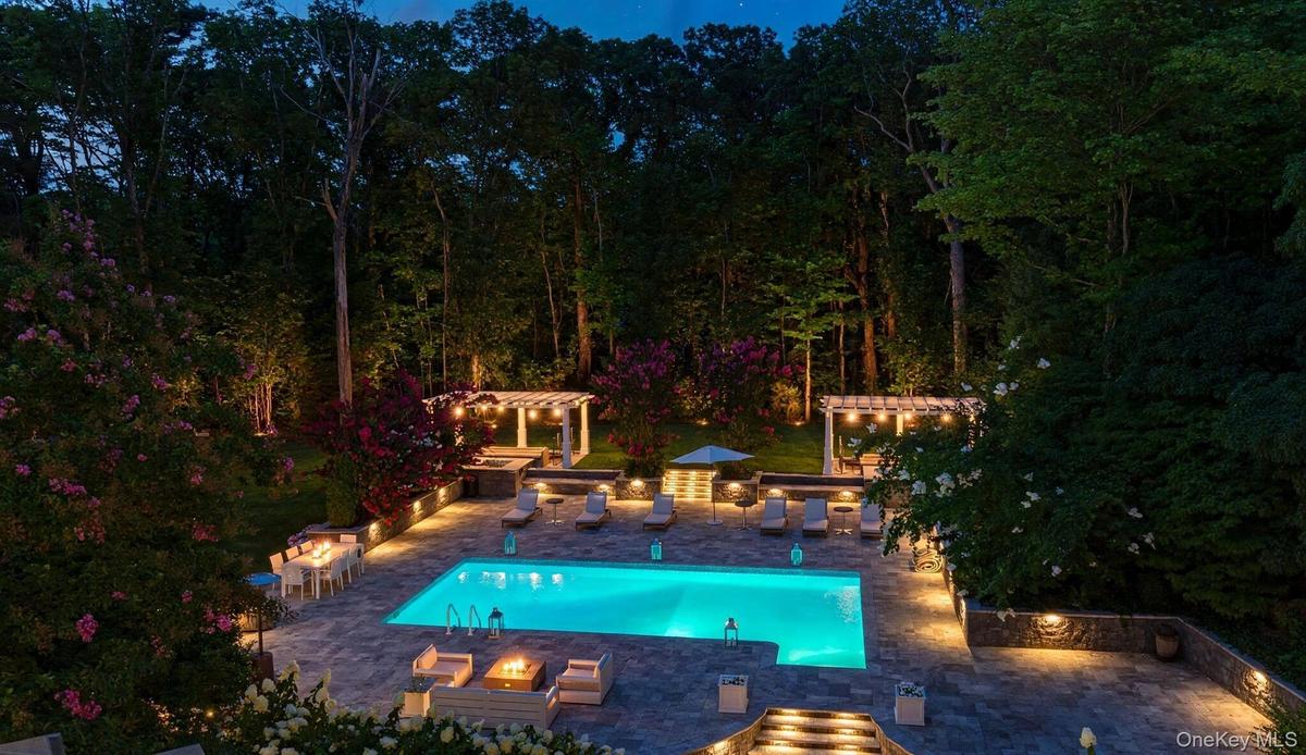 Swimming pool with paved surround, integrated fire pit, two pergolas, and recessed lighting