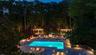 Swimming pool with paved surround, integrated fire pit, two pergolas, and recessed lighting