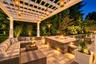 Expansive patio featuring a white pergola with hanging lanterns, a built-in stone fire pit, integrated lighting, and paver flooring