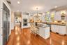 Hardwood flooring, stainless steel appliances, white cabinetry with crown molding, a kitchen island with seating, and recessed lighting