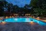 Inviting swimming pool with integrated lighting, extensive stone paver decking, retaining walls, and pergola structures