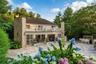 Elegant brick Colonial with a sophisticated rear elevation featuring a two-story stone facade, decorative balustrade, and expansive patio in stone-fin