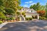 White siding exterior with a dark shingle roof, attached garage, stone retaining walls, stone steps, and mature landscaping