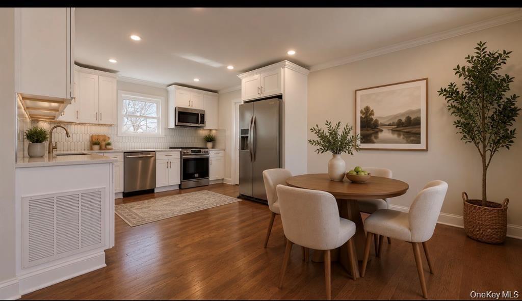 Hardwood flooring, recessed lighting, white cabinetry, stainless steel appliances, and a tiled backsplash Digitally staged