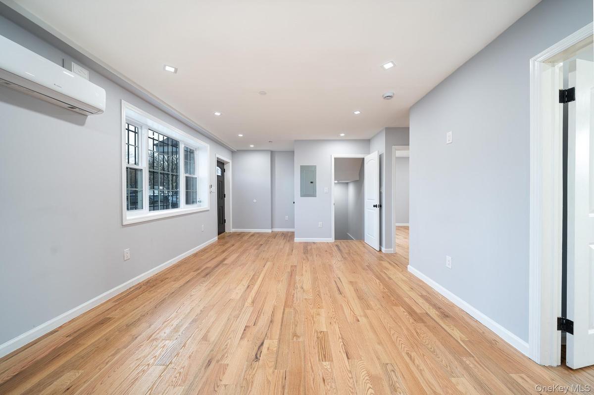 Unfurnished living room featuring a wall mounted AC, light wood-type flooring, recessed lighting, and electric panel