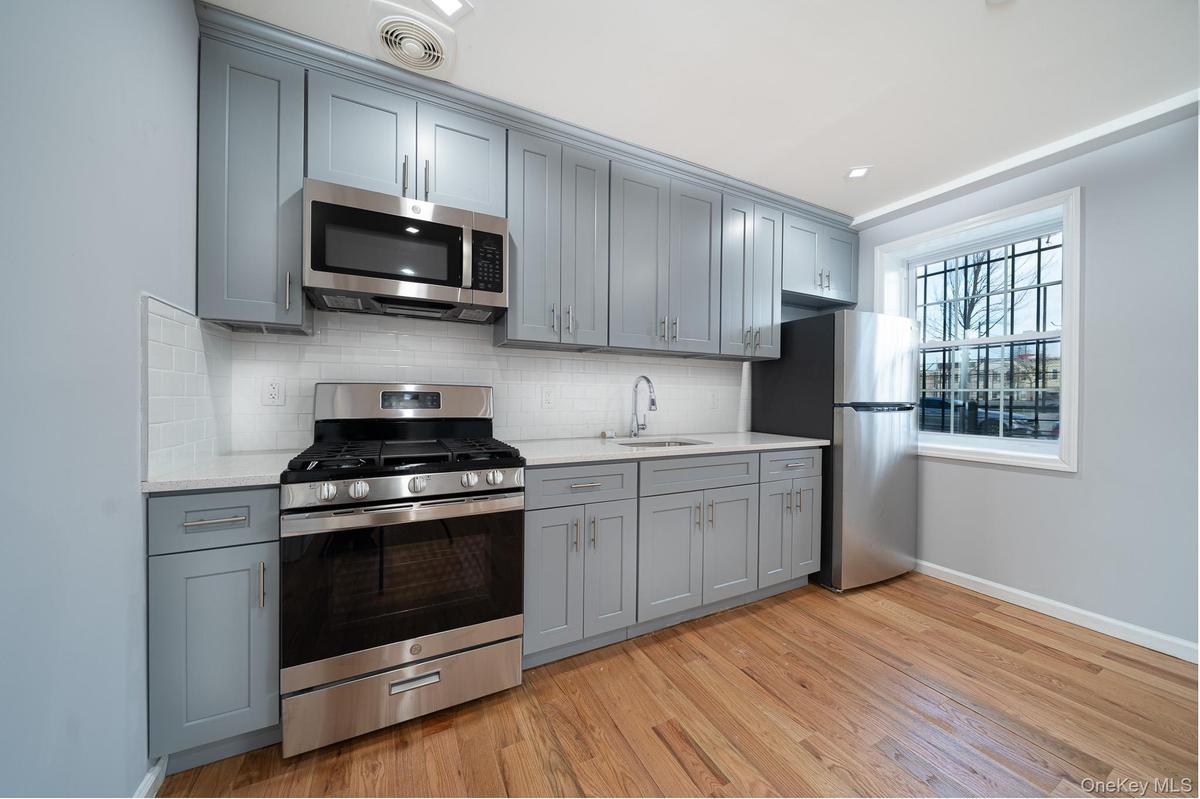 Kitchen featuring appliances with stainless steel finishes, gray cabinetry, decorative backsplash, and light stone countertops