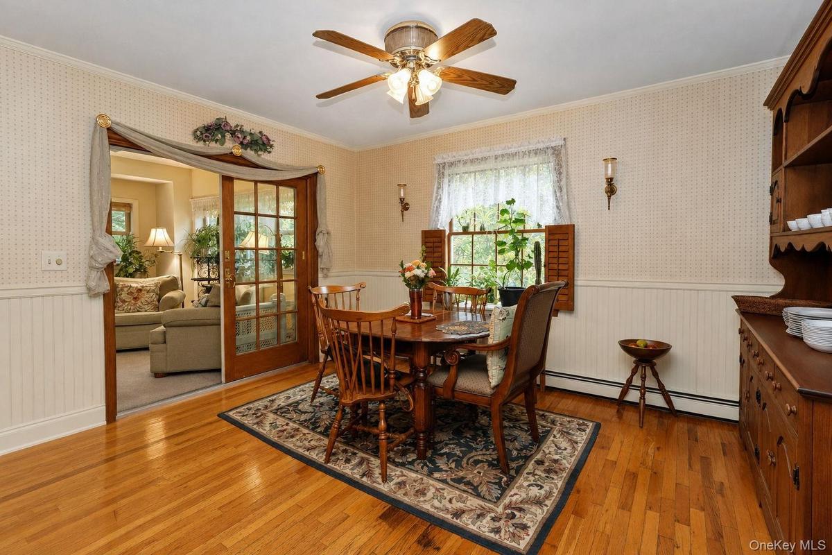 Breakfast nook hardwood flooring, paneled wainscoting, glass-paneled sliding doors, window with interior shutters, and a ceiling fan with integrated l