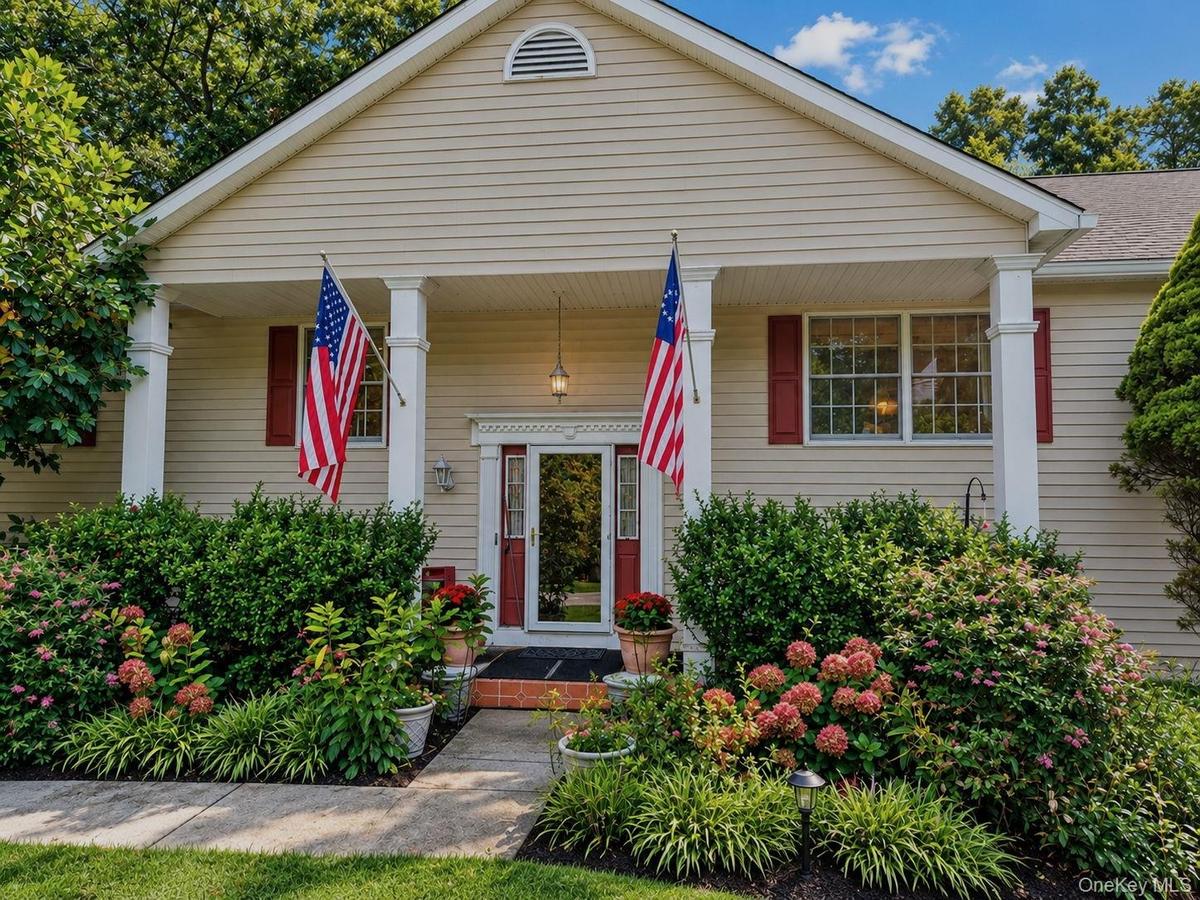 Cream-colored siding exterior with a covered porch, featuring decorative pillars and red window shutters