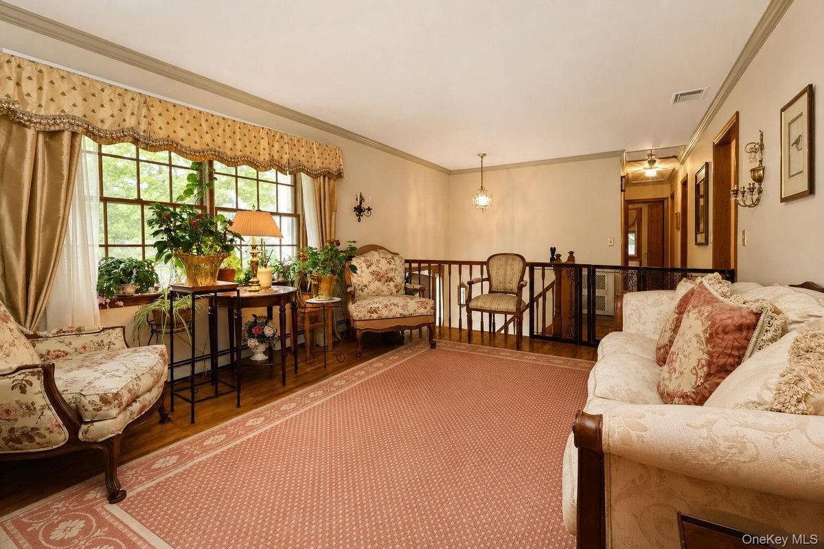 Hardwood flooring with an area rug, a built-in wall sconce, and a window with a valance wood railings