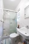 White tiled bathroom featuring a glass-enclosed shower, wall-mounted sink, and a window