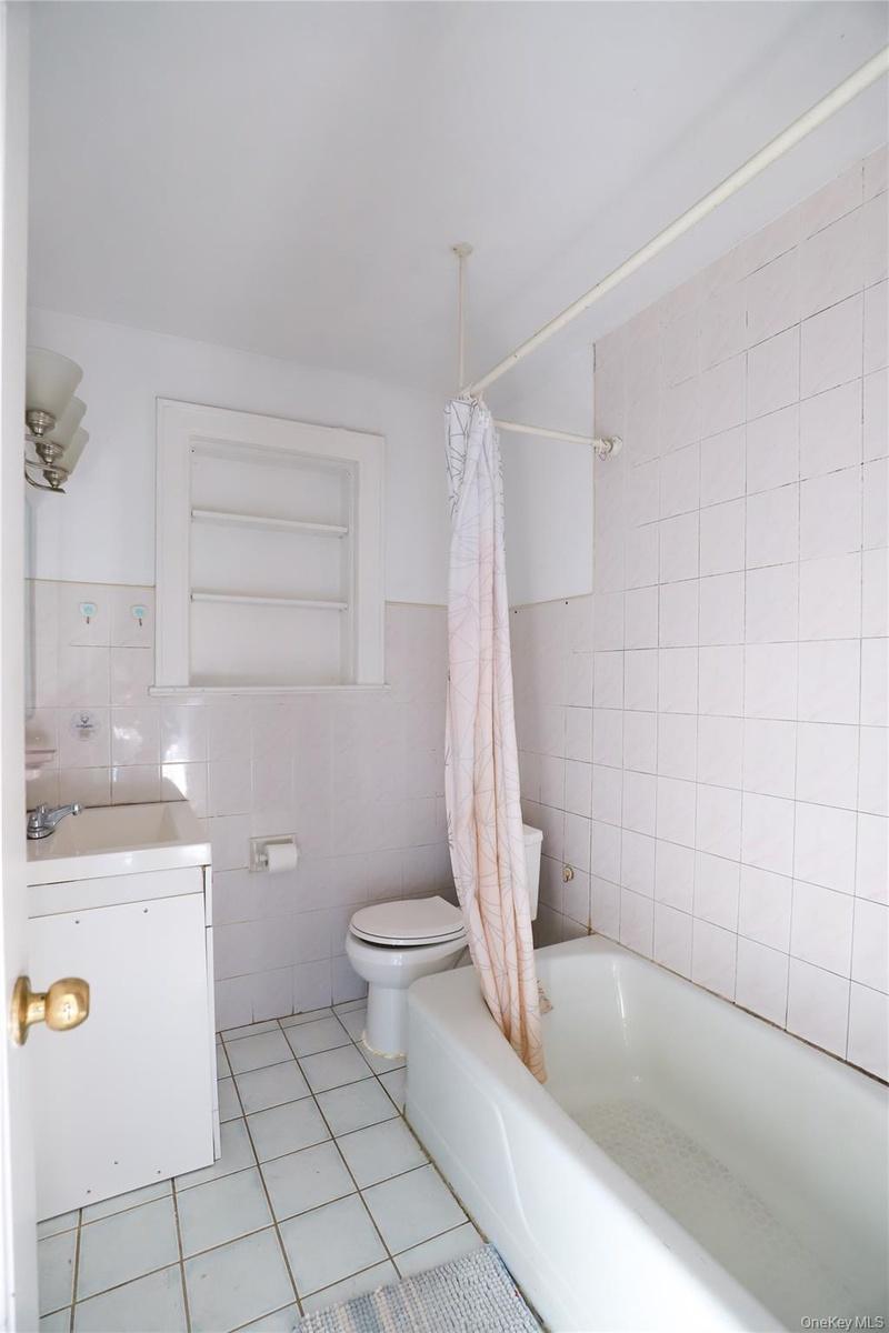 Bathroom featuring a white vanity with a porcelain sink, a toilet, and a bathtub with tile surround