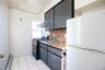Galley kitchen featuring dark cabinetry with brushed metal hardware, wood-finish countertops, tile flooring, stainless steel range hood, and white app