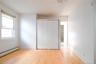 Bright, sun-filled bedroom showcasing gleaming wood-finish flooring, white painted closet doors with metal framing, and large window with natural ligh