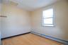 Bright corner room with wood-finish flooring, large double-hung window with natural light exposure, and clean walls with neutral finish