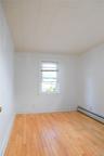 Bright, light-filled bedroom with hardwood flooring, white walls, and a large double-hung window providing natural illumination