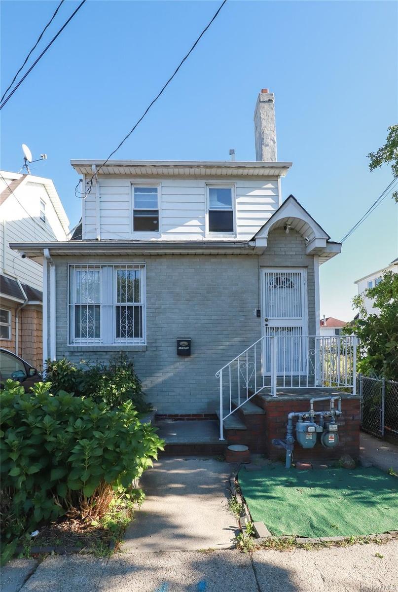 Classic two-story home featuring a brick and siding exterior, peaked roofline with chimney, and metal railing entry stairs