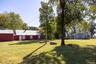 View of the barn and residence with an expansive open lawn, established trees and versatile space.