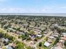 An elevated view highlights the home’s corner lot and tree-filled surroundings, with the bay forming a scenic backdrop beyond the neighborhood.