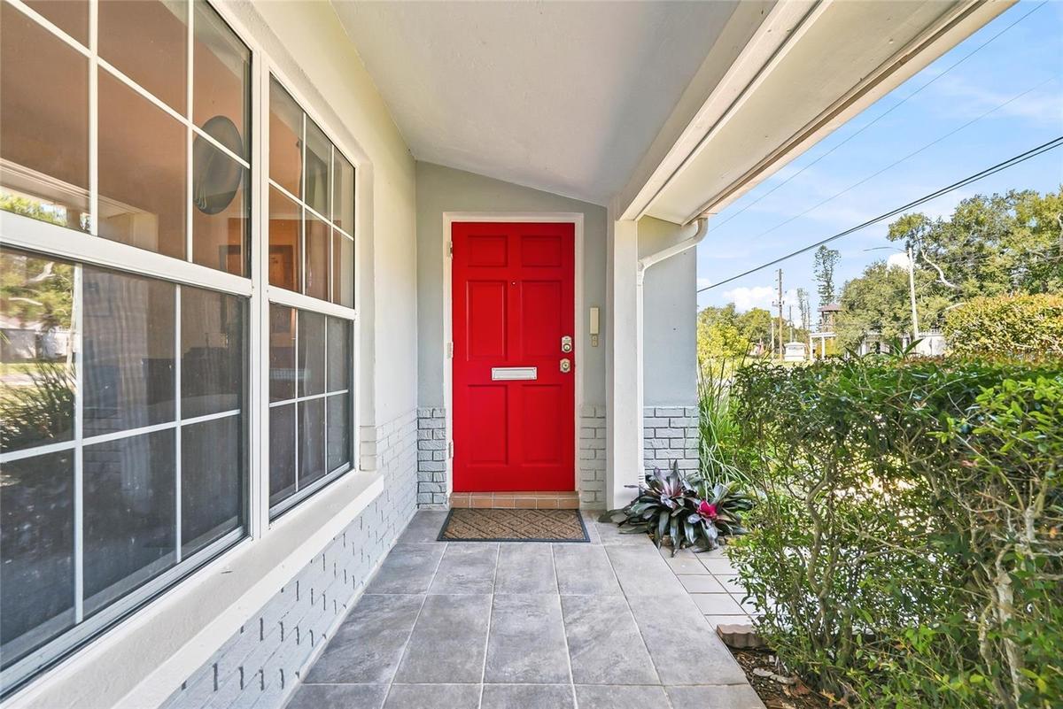 Step inside through a cheerful red front door, tucked beneath a covered, tiled porch framed by beautiful landscaping.
