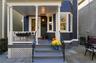 Covered front porch with white columns, wood siding exterior, bay window, stone tile patio, and wrought iron railing