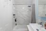 Bathroom featuring a white rectangular bathtub, white tiled shower surround with a built-in niche, modern square rain shower head, and a white rectang