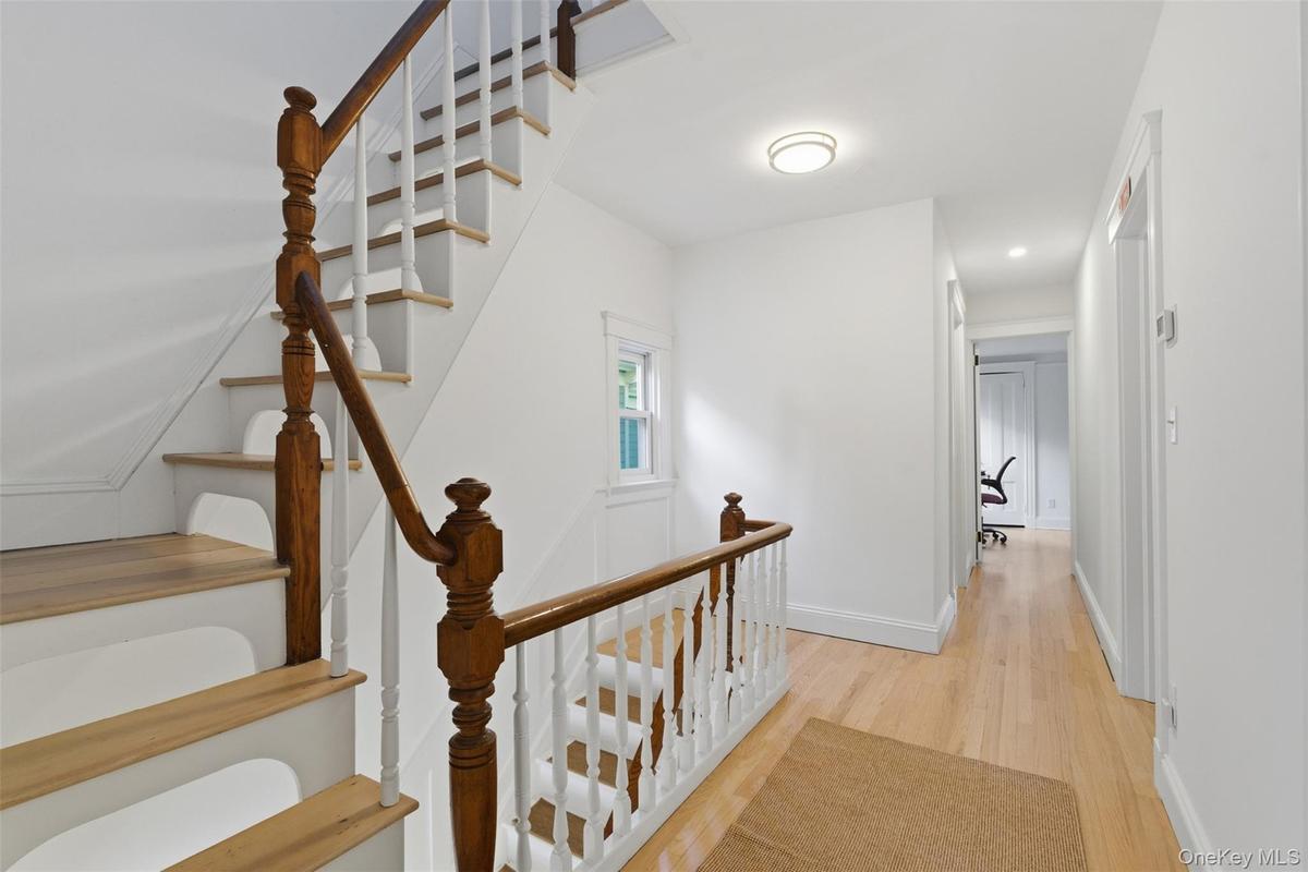 Hardwood flooring, painted white walls, wood staircase with white balusters, recessed lighting, and a window with trim