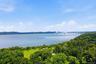 Expansive waterfront with distant bridge, lush green hills, and mature trees